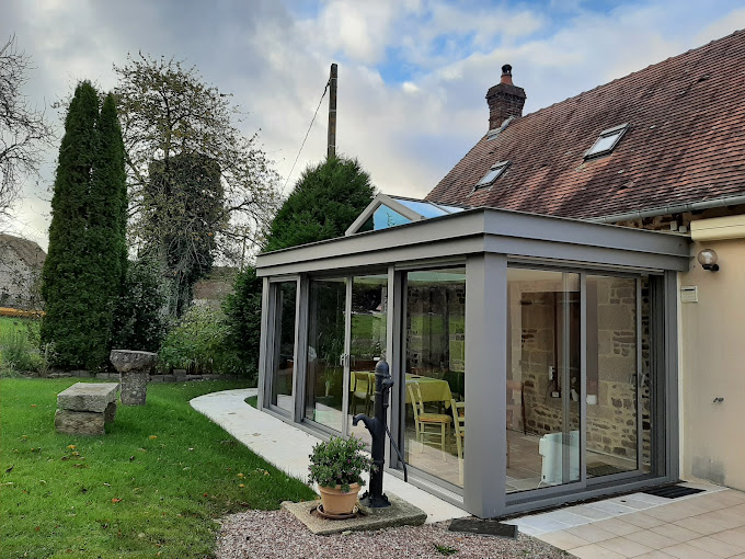 Veranda gris clair au toit plat sur une maison de campagne en normandie avec une petite terrasse non aménagée