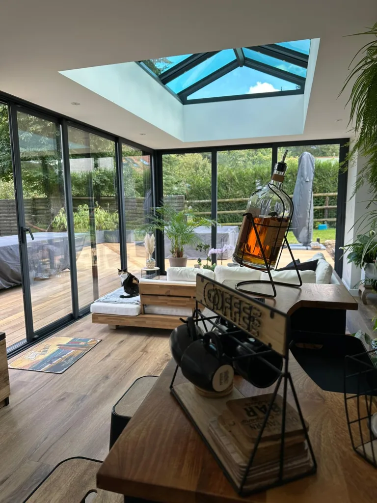 intérieur d'une extension de maison normandie concept alu avec un puit de lumière diamant. La pièce est un grand salon lumineux avec des canapés